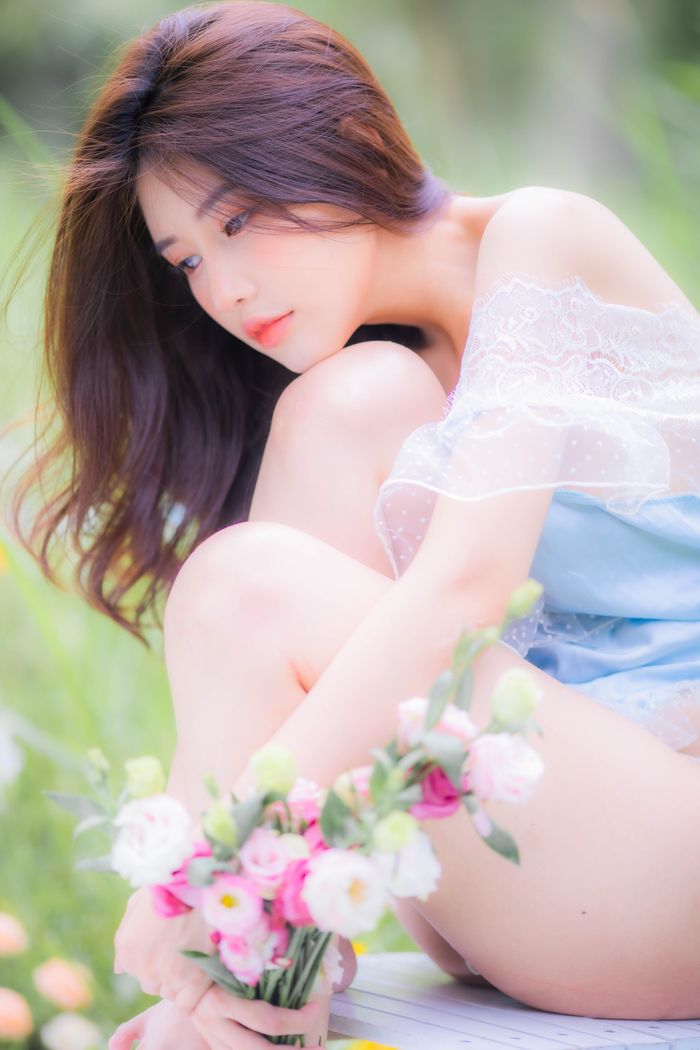 Beautiful woman sitting in a grass field with flowers, showcasing grace and tranquility.